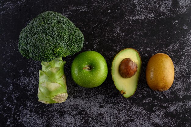 Broccoli, appel, avocado en kiwi op een zwarte cementvloer.