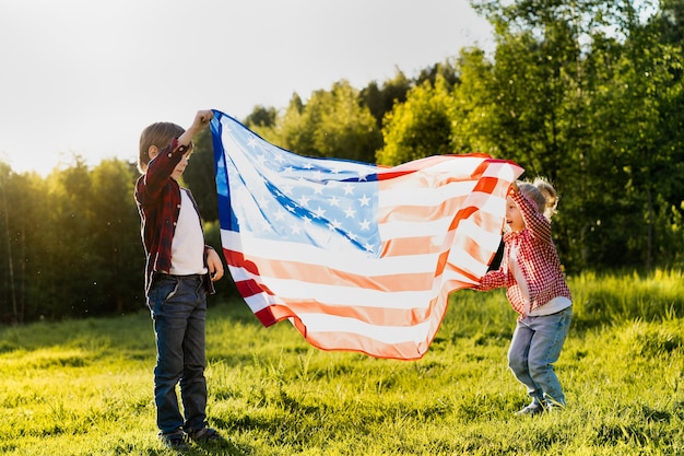 Broer en zus met de amerikaanse vlag in het zonlicht, gelukkige kinderen op de amerikaanse onafhankelijkheidsdag
