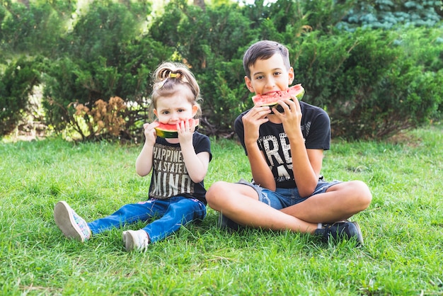 Broer en zus zitten in de tuin eten watermeloen