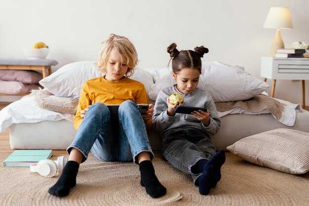 Broers en zussen in bed spelen op mobiel en tablet