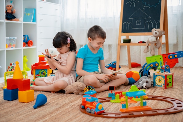 Broers en zussen, kinderen, broer en zus, vrienden zitten op de vloer, speelkamer voor kinderen met smartphones, los van het verspreide speelgoed.