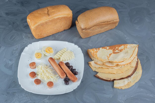 Gratis foto broodblokken en pannenkoeken naast een ontbijtschotel op marmeren tafel.