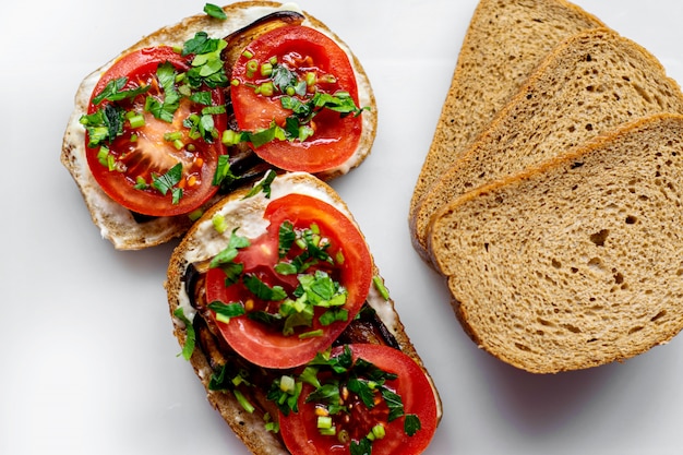Gratis foto brown toasts hete sneetjes brood samen met rode gesneden tomaten en gebakken zwarte aubergine met groenen op witte vloer