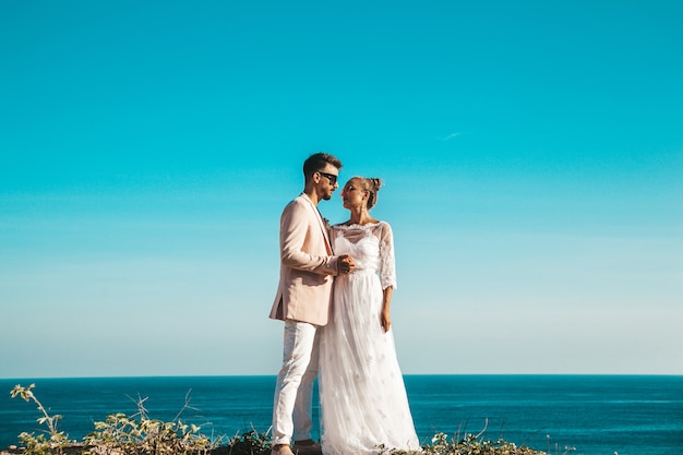 bruid en bruidegom poseren op de klif achter blauwe hemel en zee