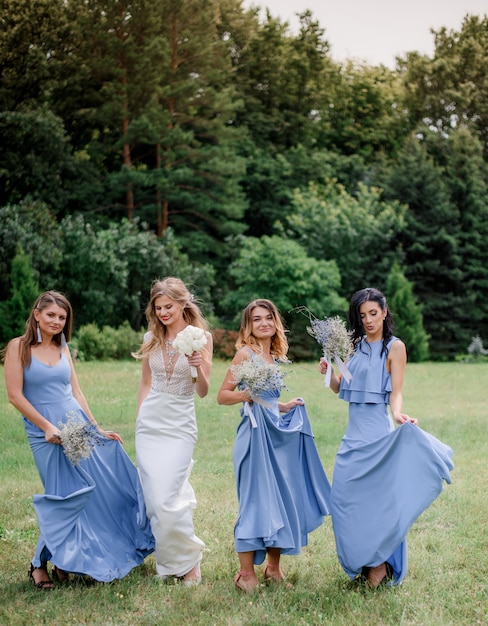 Gratis foto bruid met drie bruidsmeisjes gekleed in blauwe jurken met plezier in het groene park