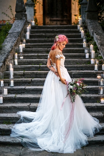 Gratis foto bruid met roze haar en tatoeages op haar tedere schouder staat op voetstappen met glanzende kaarsen