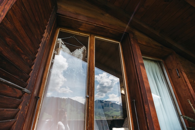 Gratis foto bruidsjurk hangt aan een raam in een enorme houten hotelkamer