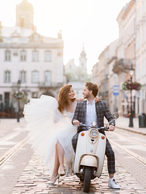 Gratis foto bruidspaar poseren op vintage scooter op straat van de oude stad