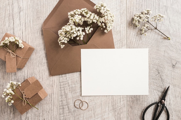 Bruine envelop met bloemen voor baby's; geschenkdozen; trouwringen; schaar en witte kaart op houten achtergrond