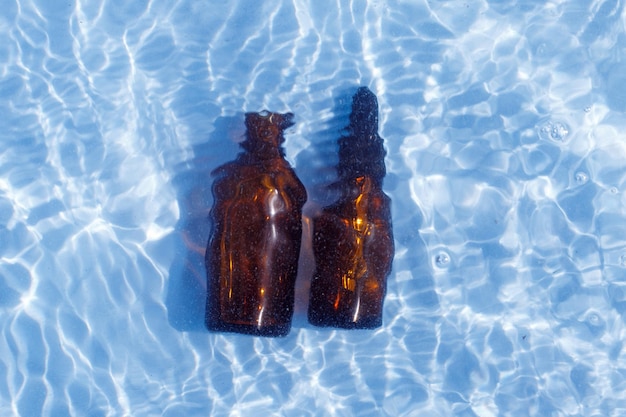 Bruine glazen oliefles onder zoet water op een blauwe achtergrond. aromatherapie en parfums concept