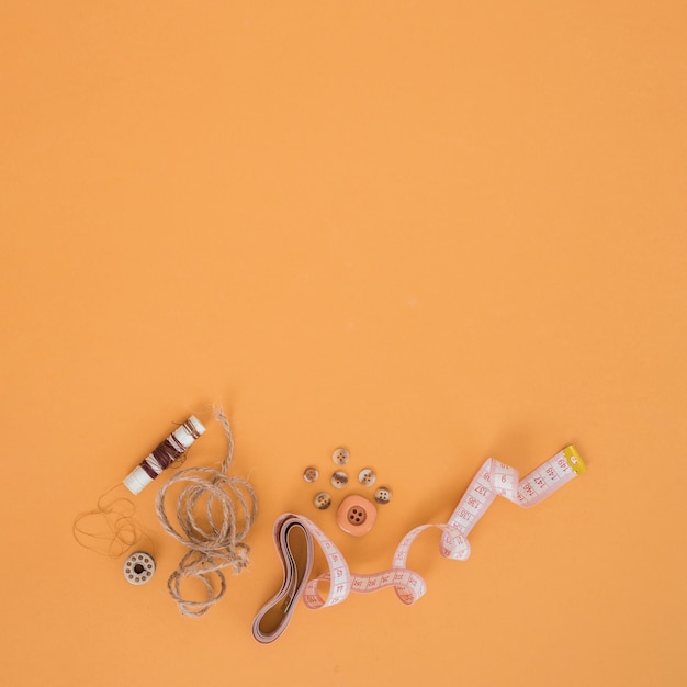 Bruine spoel; draad; knoppen en meetlint op een oranje achtergrond