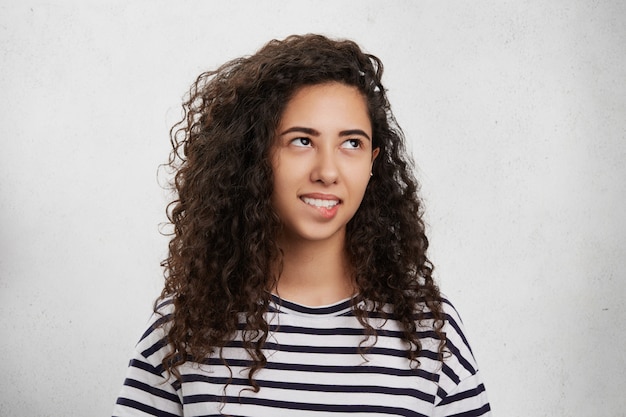 Brunette gekrulde gemengd ras vrouw bijt onderlip als onzeker en gefrustreerd, heeft een doordachte uitdrukking