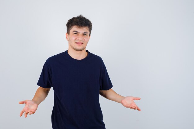 Brunette man in donkere t-shirt vragen vraag gebaar maken en op zoek ontevreden, vooraanzicht.