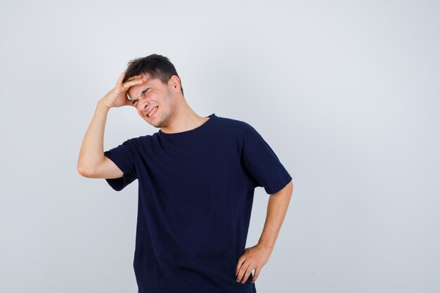 Brunette man met hand boven het hoofd in t-shirt en op zoek vrolijk. vooraanzicht.