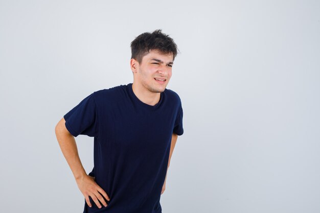 Brunette man poseren met handen op taille in t-shirt en op zoek vrolijk. vooraanzicht.