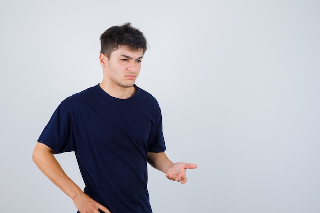 Brunette man vragen vraag gebaar maken in donkere t-shirt en op zoek verbaasd, vooraanzicht.