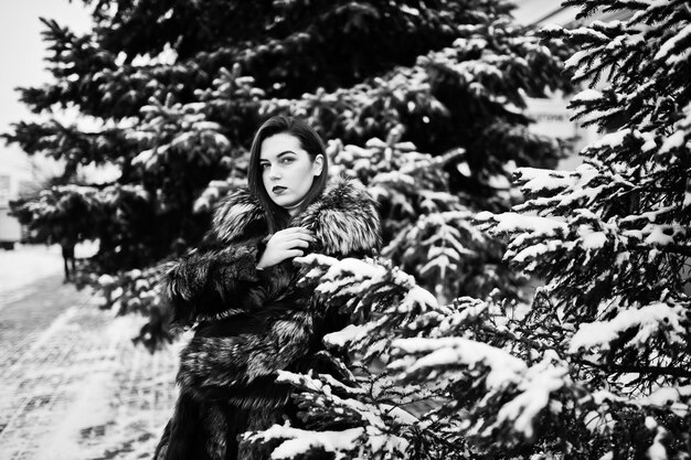 Brunette meisje in groene bontjas op winterdag tegen besneeuwde dennenboom