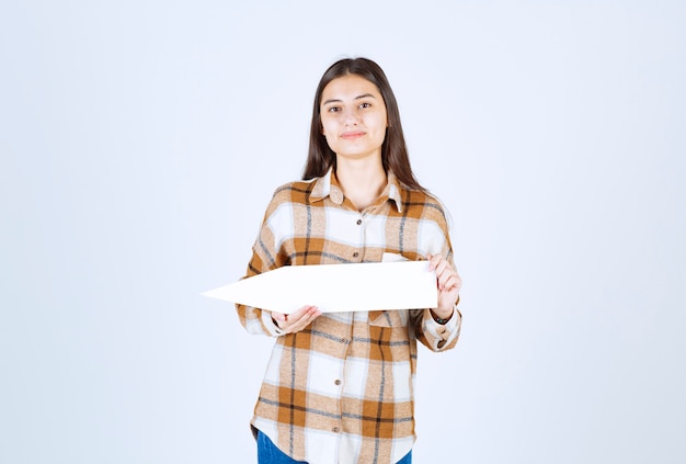 Brunette meisje poseren met lege toespraak pijlaanwijzer op witte muur.