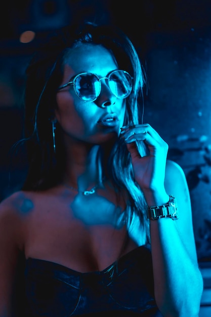 Brunette model 's nachts in de stad met blauwe leds blauwe bril en een horloge kijkend naar de camera