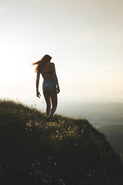 Brunette vrouw in beha en korte broek genietend van het uitzicht vanaf de top van de berg tijdens zonsondergang