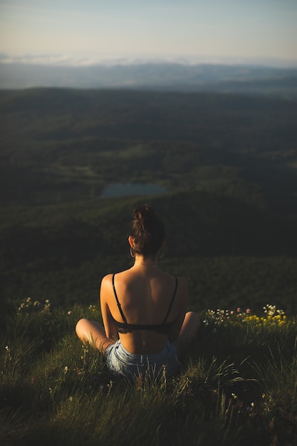 Gratis foto brunette vrouw in beha zittend op de top van de berg en genieten van het uitzicht