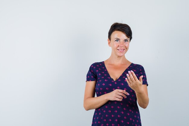 Brunette vrouw in paars en rood patroon jurk monocle maken met haar vingers en charmant, vooraanzicht op zoek.