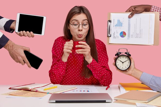 Brunette vrouw zittend aan een bureau omringd met gadgets en papieren