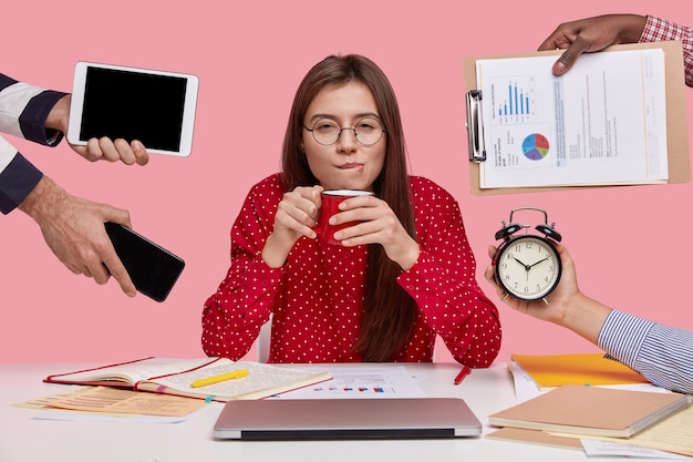 Brunette vrouw zittend aan een bureau omringd met gadgets en papieren