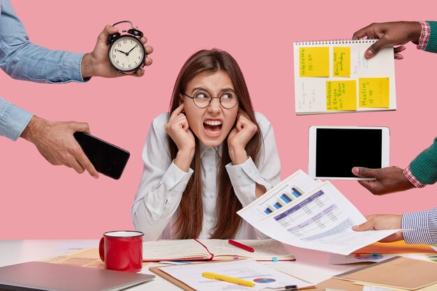 Brunette vrouw zittend aan een bureau omringd met gadgets en papieren