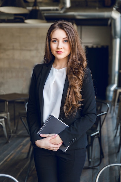 Brunette zakenvrouw met golvend lang haar en blauwe ogen staat met een notebook in handen