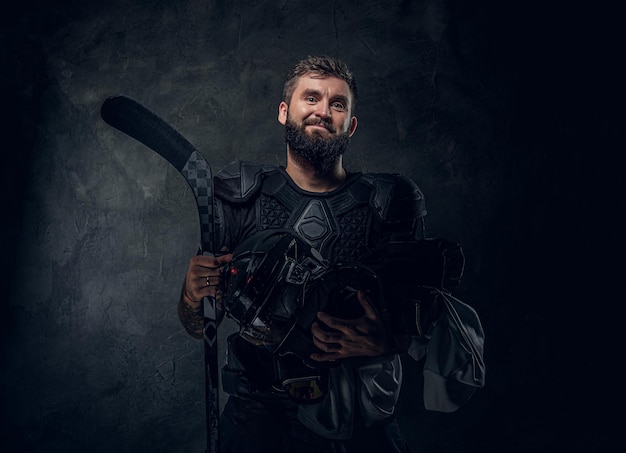 Brutale getatoeëerde hockeyspeler poseert voor fotograaf in donkere fotostudio.
