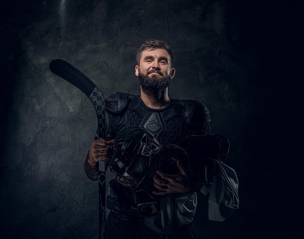 Brutale getatoeëerde hockeyspeler poseert voor fotograaf in donkere fotostudio.
