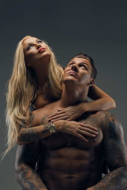 Gratis foto brutale getatoeëerde man en sexy blonde vrouw geïsoleerd op een grijze achtergrond. contrast studiolicht met schitteringen en diepe schaduwen.