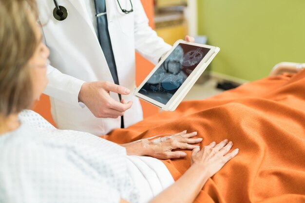 Buik van arts die xray-rapport op digitale tablet toont aan hogere patiënt in het ziekenhuis