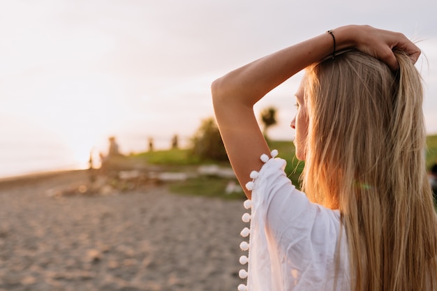 Buiten close-up portret van achterkant van jonge aantrekkelijke vrouw met blond haar ontmoet de dageraad op de oceaan