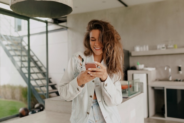 Buiten gelukkig portret van charmante vrij lachende vrouw met krullen scrollen smartphone in een modern huis met zomerterras