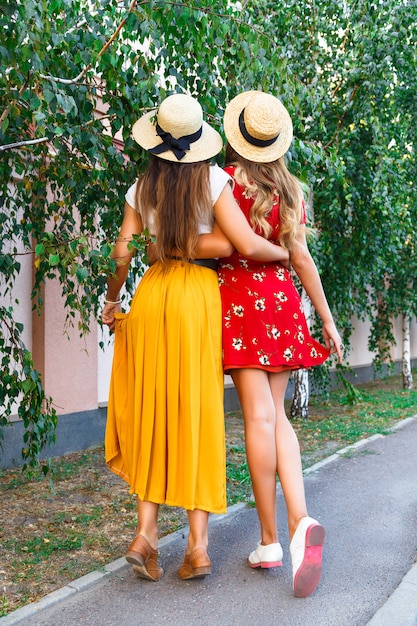 Buiten mode portret van beste vriendinnen poseren terug en knuffels, beide dragen stijlvolle trendy hipster retro jurken en hoeden. Geniet van hun vriendschap en geweldige tijd samen.