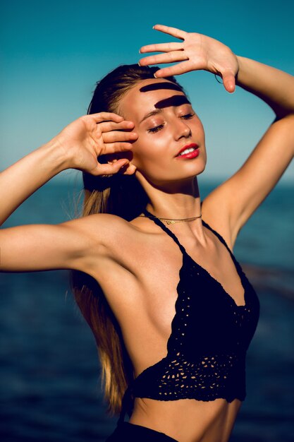 Buiten mode portret van fit tan perfecte vrouw in stijlvolle zwarte gebreide badmode poseren op het strand.