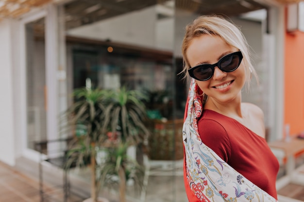 Buiten portret van schattige gelukkige blonde dame zonnebril en sjaal dragen