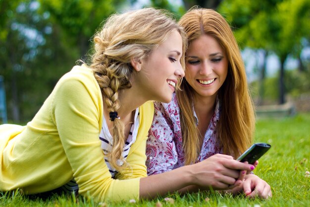 Buiten Portret van twee mooie jonge vrouwen met mobiel in het park