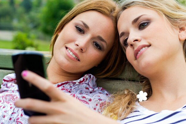 Buiten Portret van twee mooie jonge vrouwen met mobiel in het park