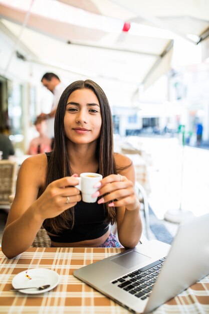 Buiten werken. Mooie jonge vrouw in funky hoed bezig met laptop en lachend zittend buiten