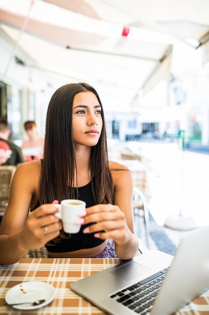 Buiten werken. Mooie jonge vrouw in funky hoed bezig met laptop en lachend zittend buiten