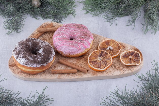 Bundel van gedroogde stukjes sinaasappel, donuts en kaneelstokjes op een bord op een witte ondergrond