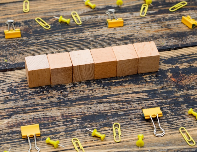 Bureauconcept met houten kubussen, paperclippen, bindmiddelenklemmen op houten achtergrond hoge hoekmening.