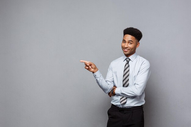 Businessconcept zelfverzekerde doordachte jonge Afro-Amerikaanse wijzende vinger aan kant over grijze achtergrond