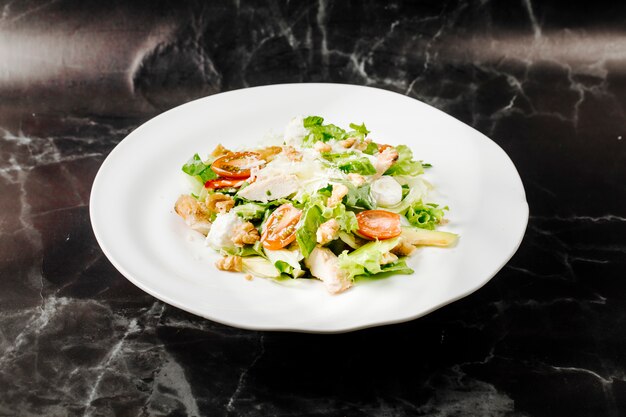 Caesarsalade met gemengde ingredienst binnen witte plaat op een zwart marmer.