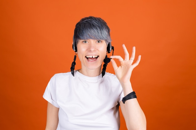 Callcenterassistent met koptelefoon op oranje muur ziet er gelukkig en positief uit met een zelfverzekerde glimlach