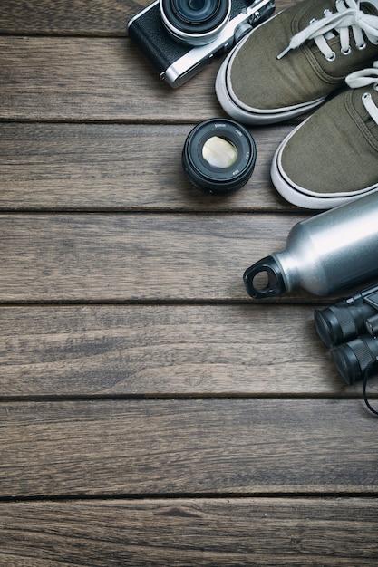 Camera, lens, verrekijker, canvas schoenen, sportfles op de retro houten tafel