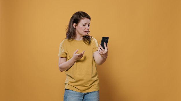 Casual gelukkige vrouw in videogesprekconferentie met smartphone die hallo zwaait naar de camera aan de voorkant in de studio. Glimlachende persoon die haar repareert en een online gesprek voert met behulp van de berichten-app voor mobiele telefoons.